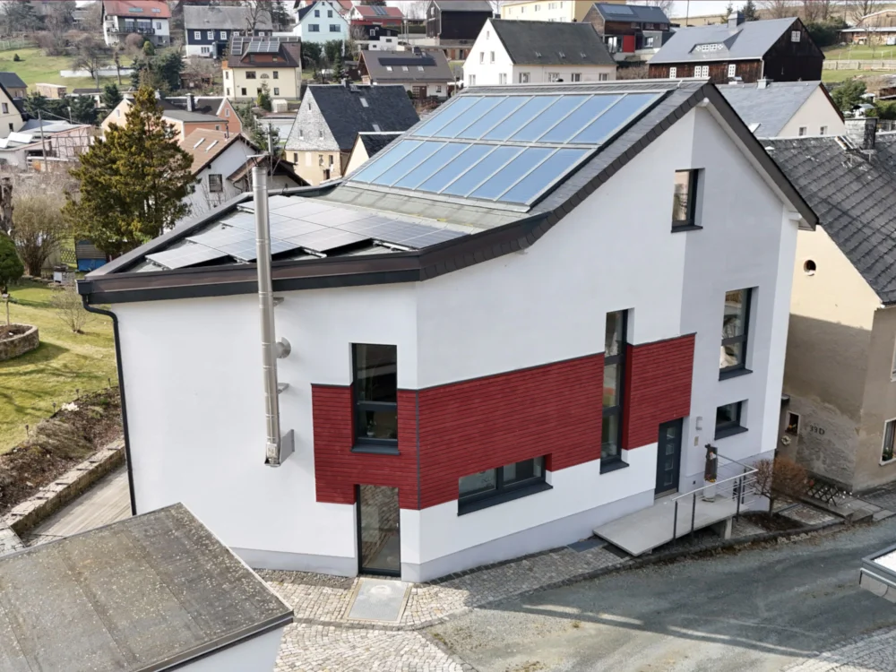 Modernes Einfamilienhaus mit Photovoltaikanlage auf dem Dach und integrierter Solartechnik, kombiniert mit rot-weißer Fassadengestaltung in ruhiger Wohngegend.