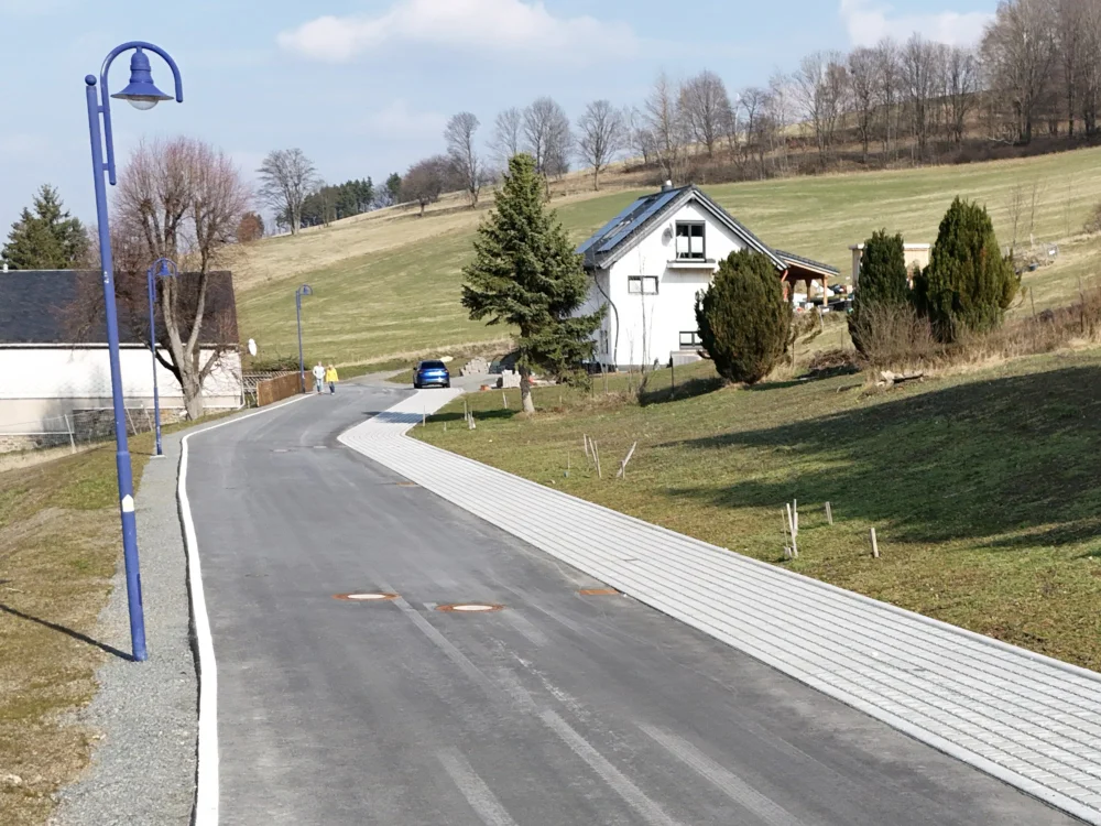 Drohnenaufnahme einer kurvigen Straße mit angrenzendem Grundstück, Baumbestand und Gewerbefläche in ländlicher Umgebung.