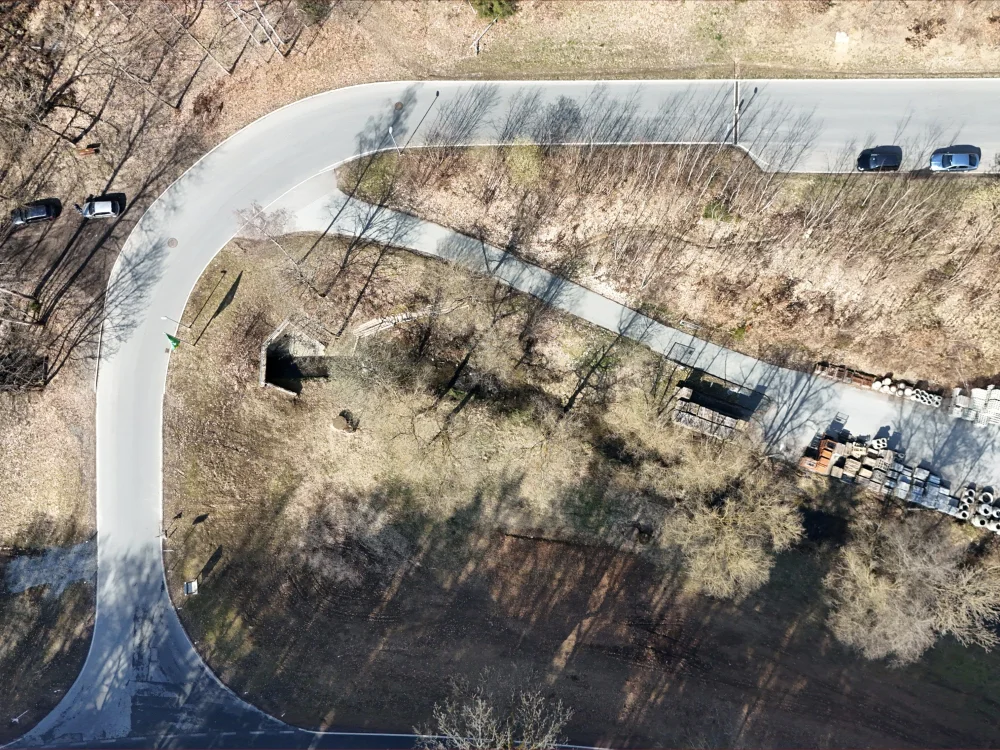 Drohnenaufnahme einer kurvigen Straße mit angrenzendem Grundstück, Baumbestand und Gewerbefläche in ländlicher Umgebung.
