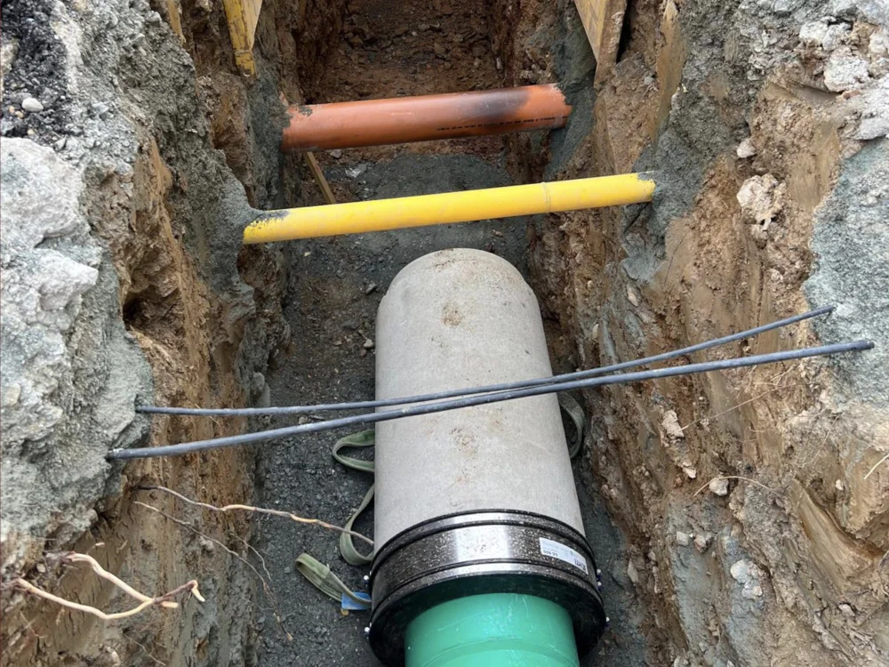 Tiefbauarbeiten im Kabel- und Rohrleitungsbau mit verlegten Schutzrohren und Abwasserleitung in offenem Graben für Hausanschluss.