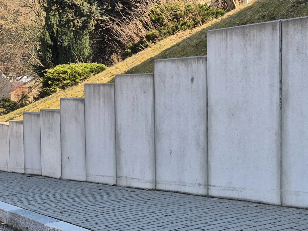 Stützmauer aus Beton-Winkelstützelementen zur Böschungssicherung mit gepflastertem Gehweg und Hangbefestigung im Außenbereich.