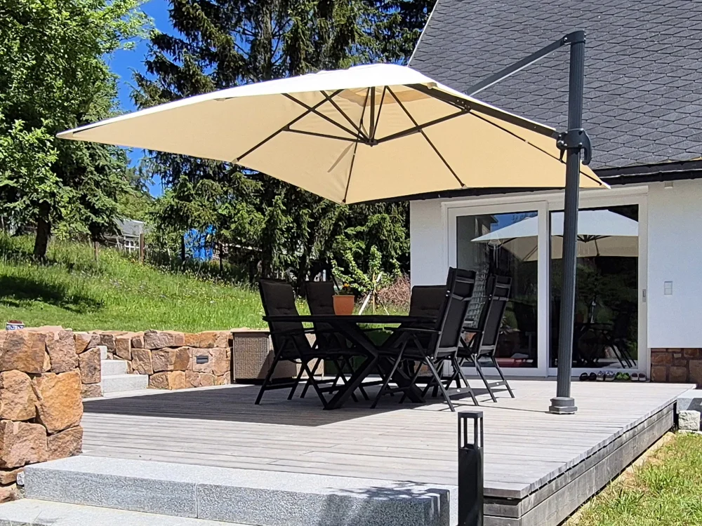 Moderne Holzterrasse mit Terrassendielen, Sitzgruppe und Sonnenschirm vor Einfamilienhaus, kombiniert mit Natursteinmauer und Gartenanlage.