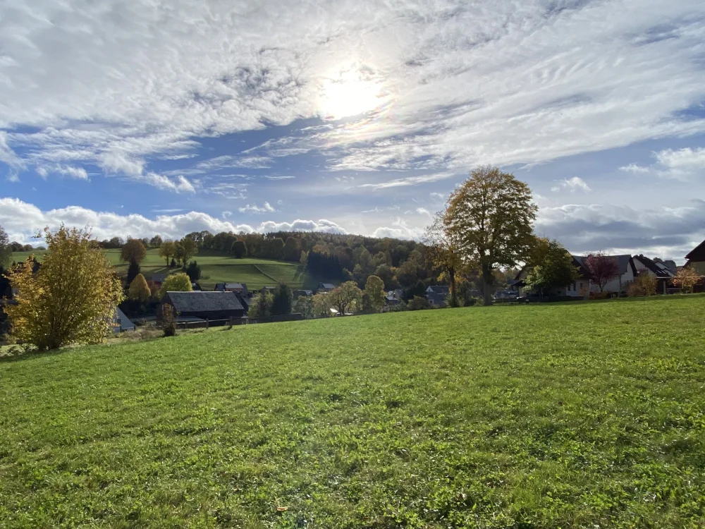 Weitläufiges Baugrundstück in ländlicher Lage mit Blick über grüne Wiesen und bestehende Wohnbebauung, ideal für Neubauprojekt oder Immobilienentwicklung.
