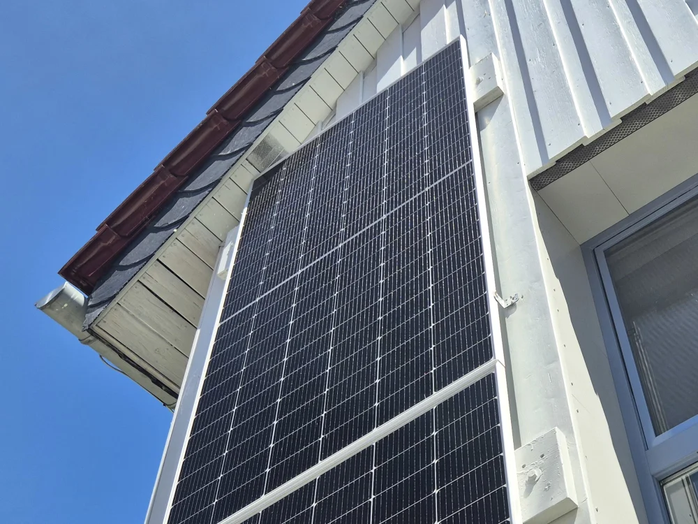 Fassadenintegrierte Photovoltaikanlage an Wohnhaus mit Holzverkleidung und Steildach, moderne Lösung zur nachhaltigen Energiegewinnung.