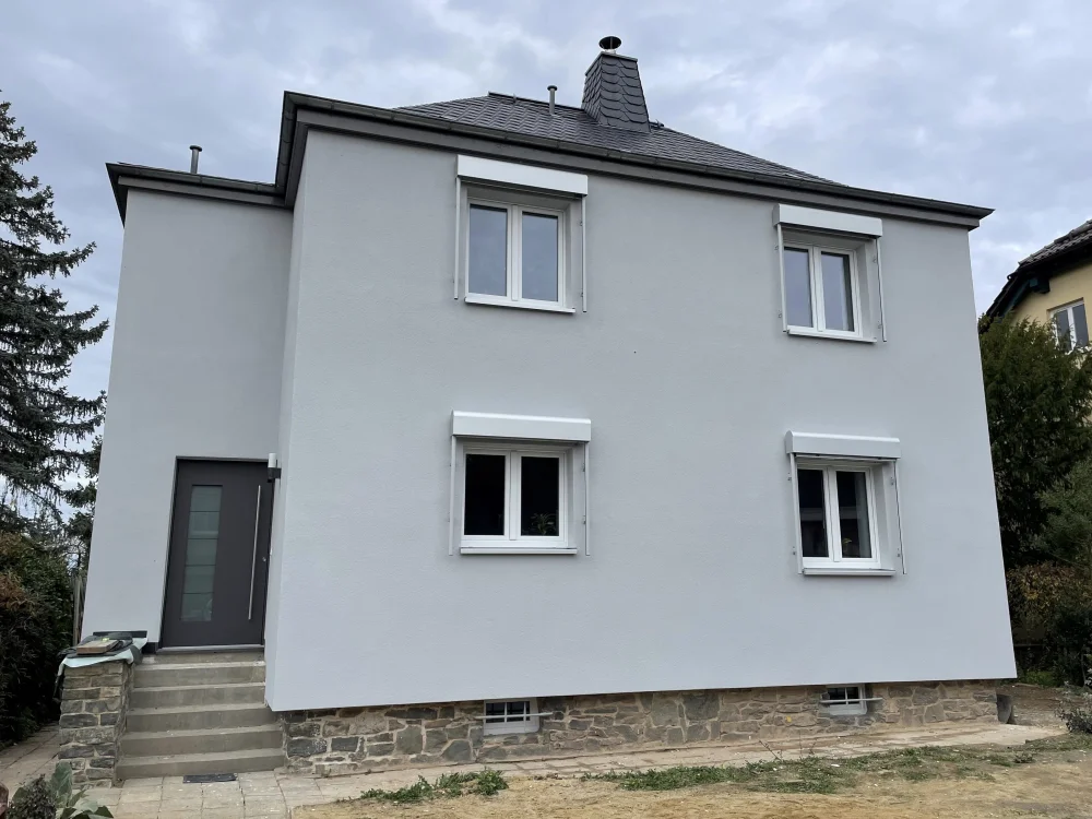 Modernisiertes Einfamilienhaus mit frisch gedämmter und verputzter Fassade (WDVS), neuen Fenstern und überarbeitetem Eingangsbereich nach energetischer Sanierung.