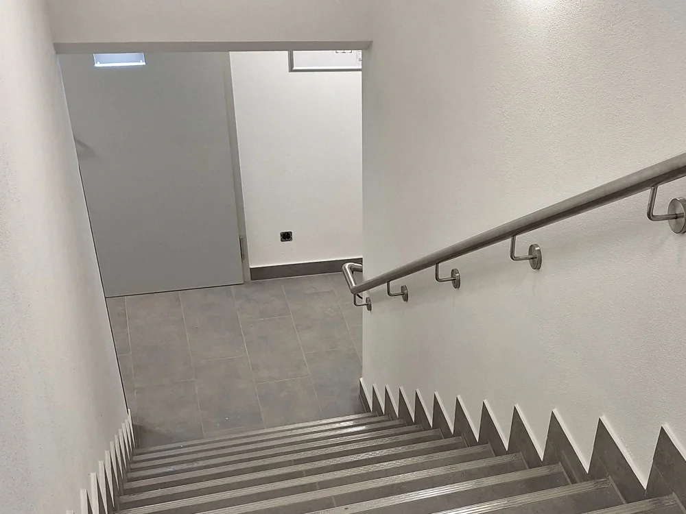 Treppenhaus im Innenbereich mit rutschfesten Stufen, Edelstahl-Handlauf und moderner Wandgestaltung, barrierearme Ausführung im öffentlichen oder gewerblichen Gebäude.