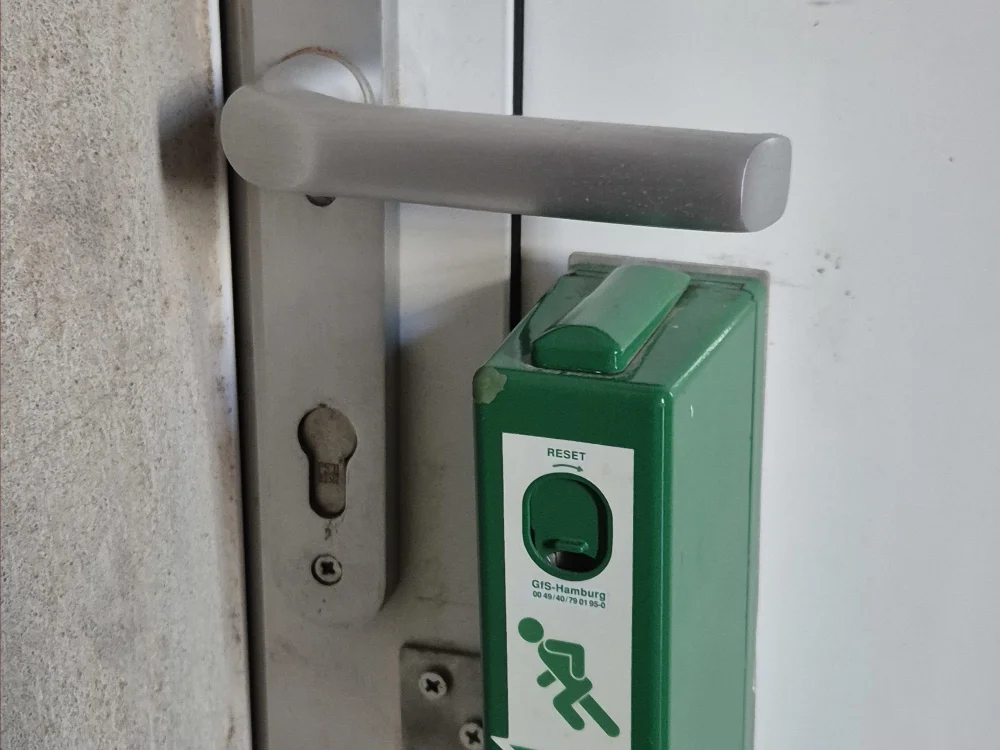 Notausgangstaster an Tür mit Panikschloss und Türgriff im Innenbereich, sicherheitsrelevante Ausstattung für Flucht- und Rettungswege nach Brandschutzvorschriften.