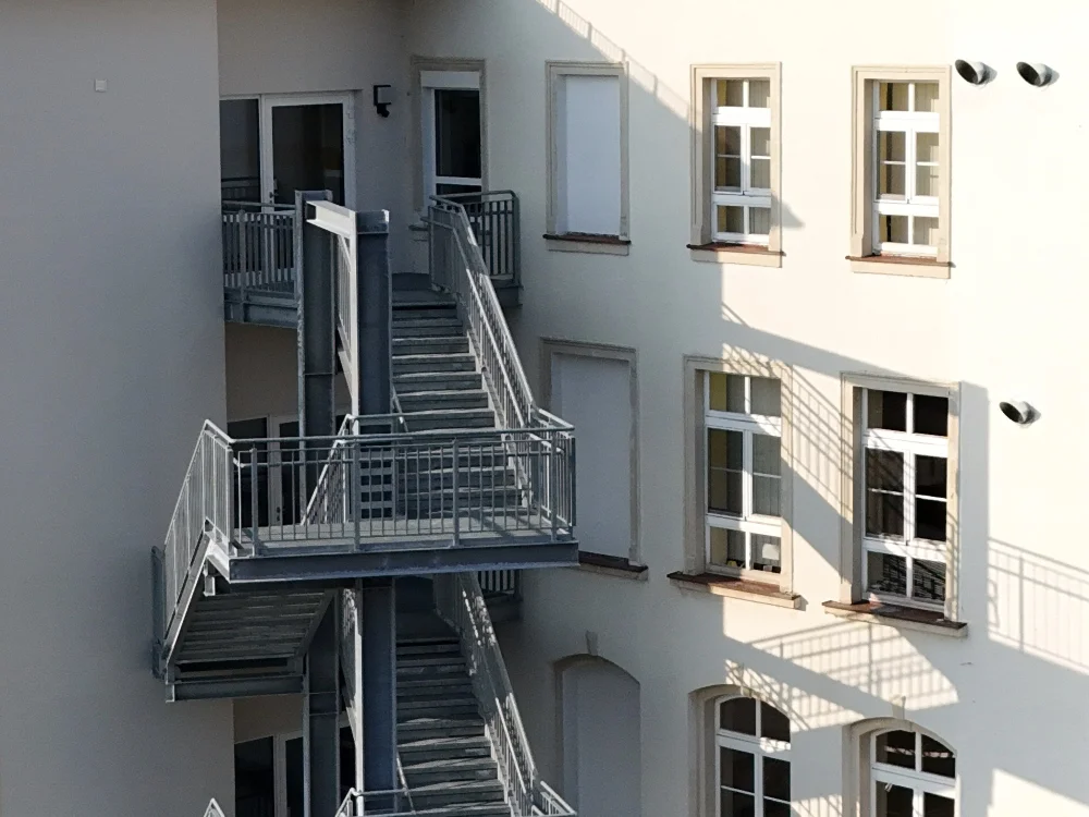 Außentreppe aus Stahl mit Geländer an Gebäudefassade, Fluchttreppe als zweiter Rettungsweg gemäß Brandschutzvorschriften im öffentlichen Gebäude.