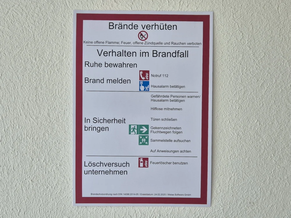 Brandschutzordnung mit Verhaltensregeln im Brandfall, Notruf 112, Fluchtweg-Hinweisen und Feuerlöscher-Nutzung, gut sichtbar an Innenwand angebracht.