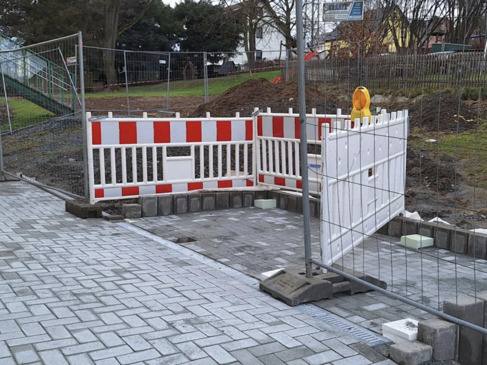 Baustellenabsperrung mit rot-weißen Schutzgittern und Bauzaun zur Sicherung von Tiefbauarbeiten auf gepflasterter Fläche im Außenbereich.