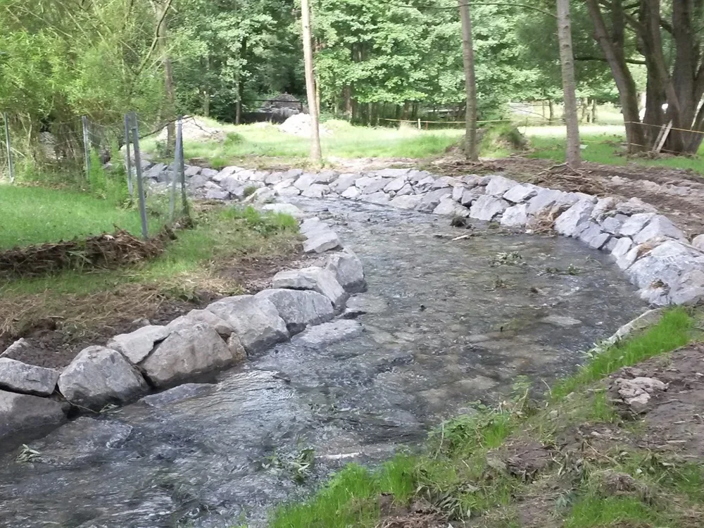 Renaturierter Bachlauf mit Natursteinverbau und gesicherter Uferböschung zur Hochwasserregulierung und Erosionskontrolle im naturnahen Wasserbau.