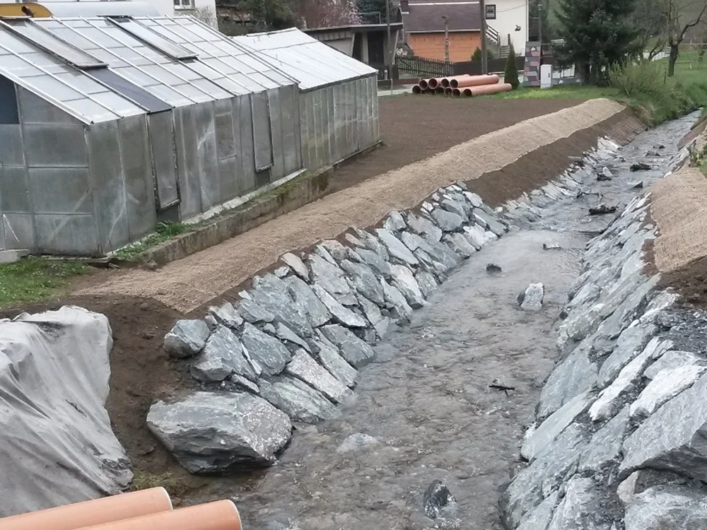 Renaturierter Bachlauf mit Natursteinverbauung und Uferbefestigung zur Hochwasser- und Erosionssicherung im Bereich Wasserbau und Landschaftsbau.