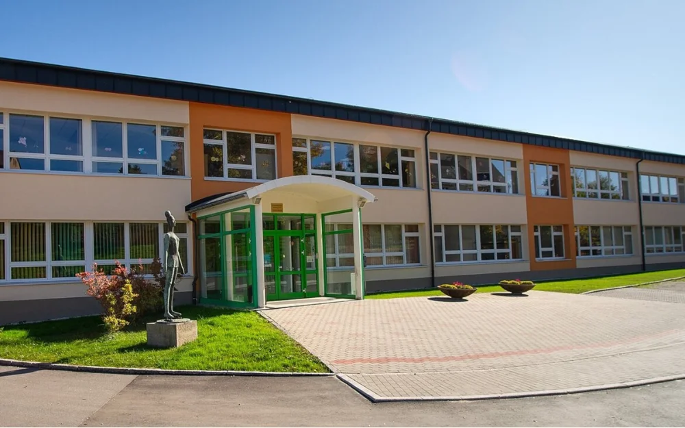 Modernisierte Grundschule mit neu gestaltetem Eingangsbereich, barrierefreier Zugangslösung und gepflegten Außenanlagen vor Schulgebäude in Neudorf.