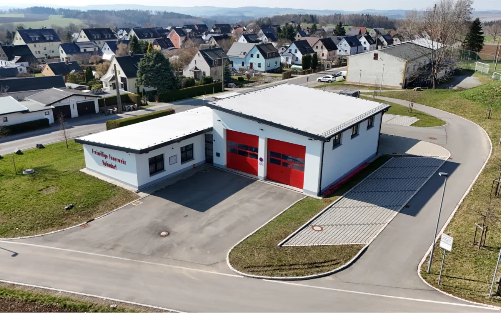 Drohnenaufnahme eines modernen Feuerwehrgebäudes mit Fahrzeughalle, Zufahrt und befestigten Außenanlagen in Wohngebiet, Standort der Freiwilligen Feuerwehr Hohndorf.
